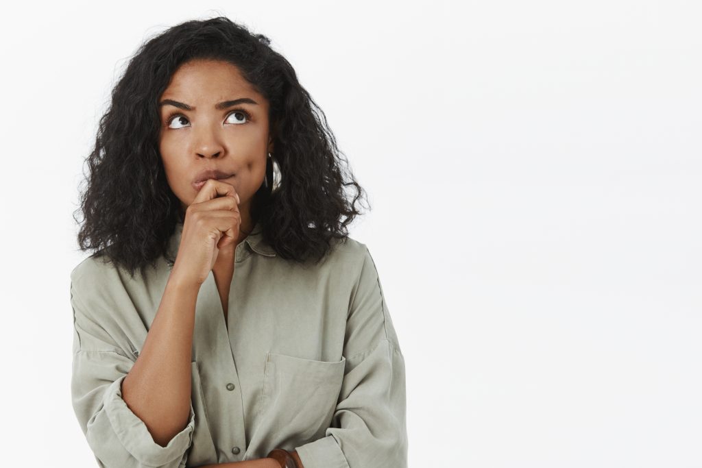 girl needs make up excuse thinking standing focused in thoughtful pose holding hand on chin frowning looking up posing over gray background determined and concentrated on thought